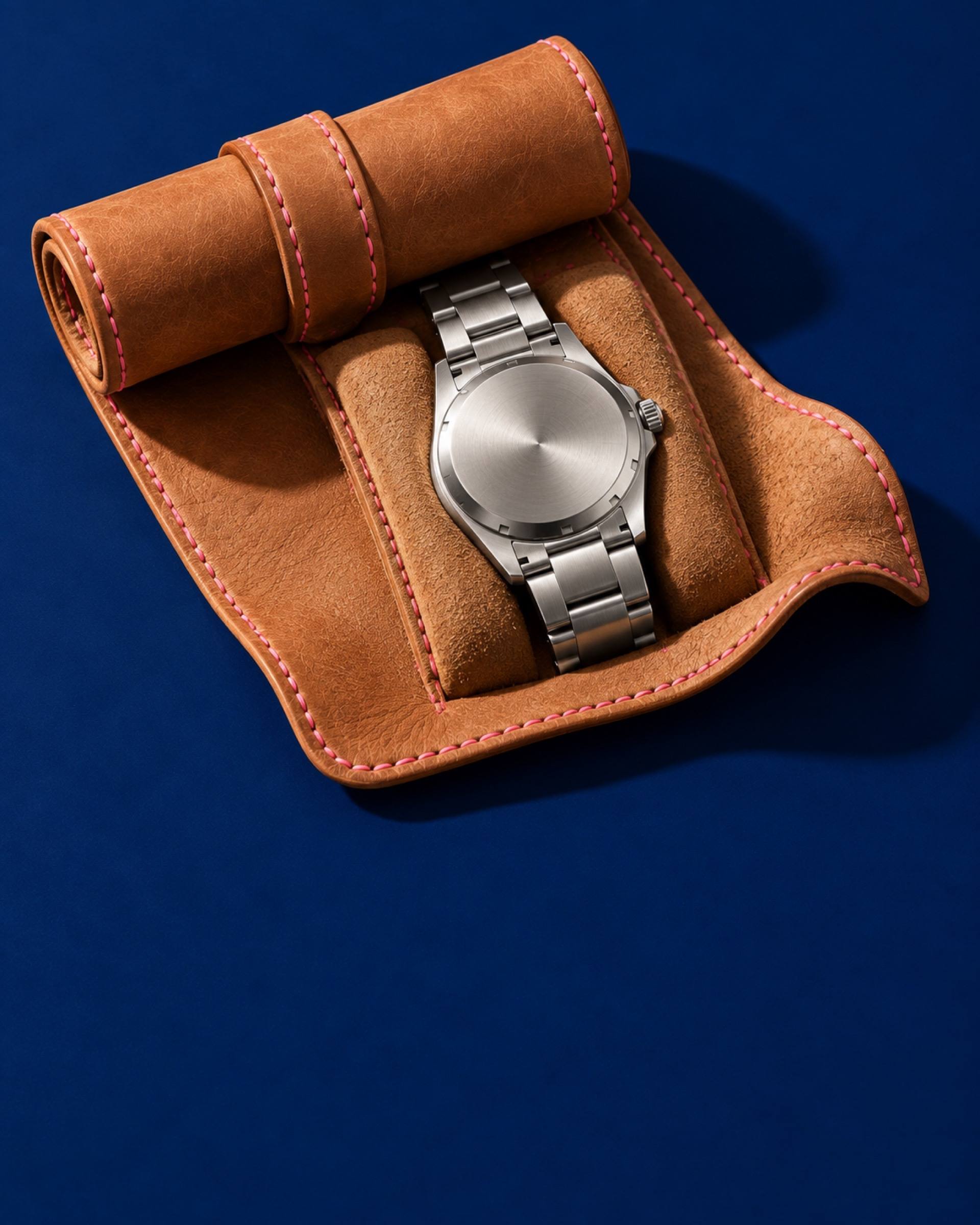 A steel watch in an open leather watch roll with pink stitching